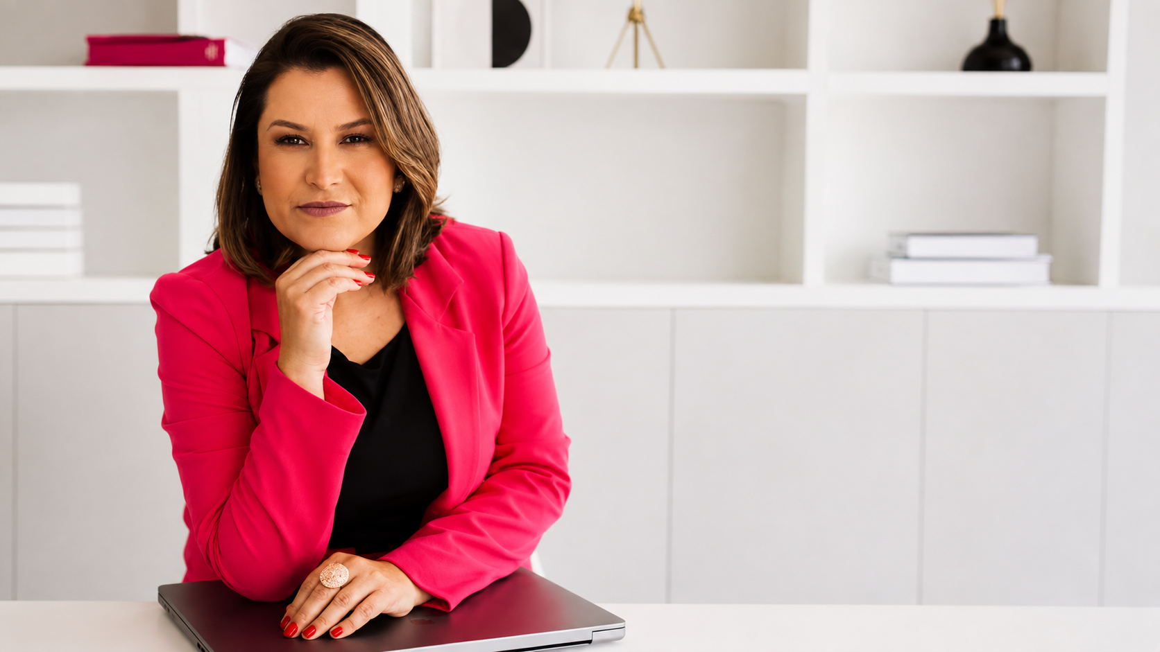 Karin Rost, de blazer rosa, apoiada sobre a mesa do escritório em Parobé.
